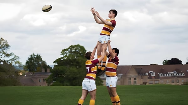 Zwei Schüler der Downside School spielen Rugby auf einem Sportfeld mit Bäumen im Hintergrund.