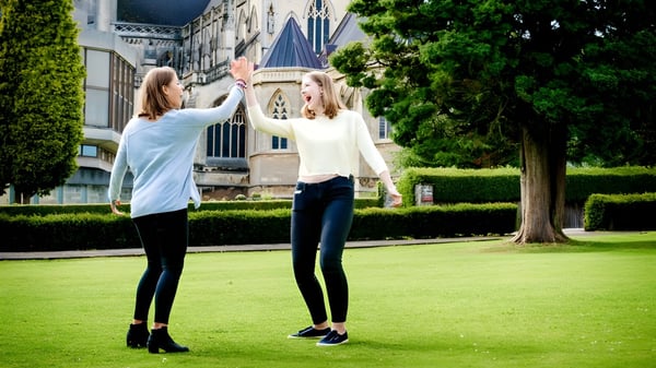 Zwei Schülerinnen stehen auf einer Wiese vor einem historischen Gebäude auf dem Gelände der Downside School.