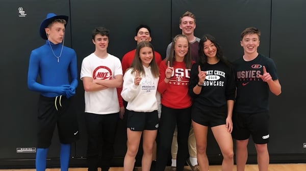 Eine Gruppe von Schülerinnen und Schülern der Dr. Frank J. Hayden Secondary School posiert vor einem dunklen Hintergrund in sportlicher Kleidung.