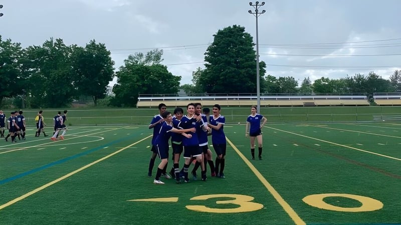 Eine Gruppe von Schülerinnen und Schülern der Dr. G.W. Williams Secondary School versammelt sich auf einem Sportfeld neben einem Stadion.
