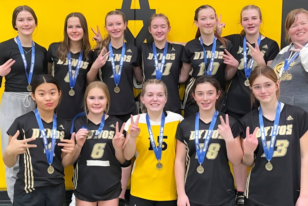 Eine Gruppe junger Athletinnen der Drumheller Valley School posiert mit Medaillen vor gelbem Hintergrund.