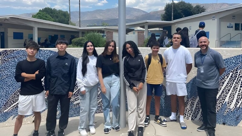 Eine Gruppe Schülerinnen und Schüler steht vor einem Gebäude mit Bergen im Hintergrund auf dem Gelände des Duarte Unified School District.