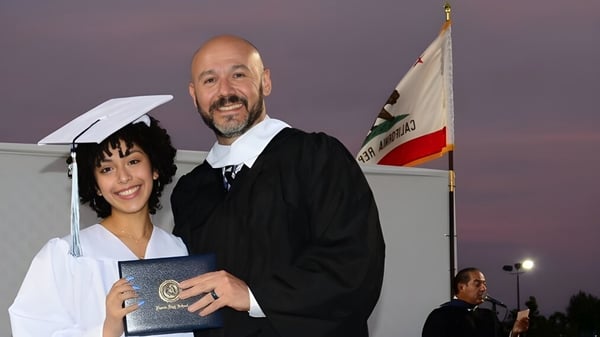 Ein Mann und eine Frau in Abschlussrobe stehen bei einer Abschlussfeier im Duarte Unified School District vor einer Flagge.