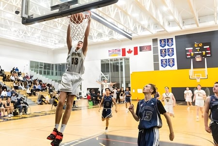 Ein Basketballspiel findet in der Sporthalle der Duchess Park Secondary School mit Spielern auf dem Spielfeld und Zuschauern auf den Tribünen statt.