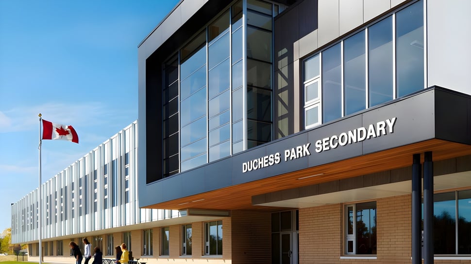 Das moderne mehrstöckige Gebäude der Duchess Park Secondary School mit großen Glasfenstern unter blauem Himmel und einer kanadischen Flagge im Vordergrund.