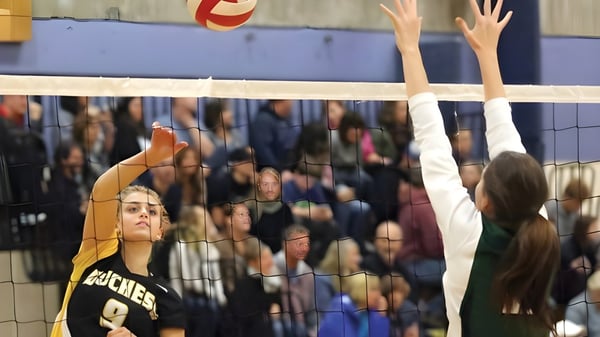 Schüler der Duchess Park Secondary School spielen Volleyball während Zuschauer im Hintergrund das Spiel verfolgen.