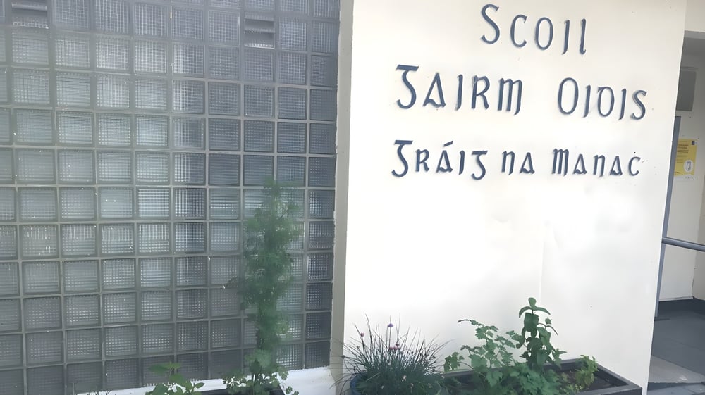 Ein Schild mit fremdsprachlichem Text vor einer Glasbausteinwand auf dem Gelände des Duiske College.