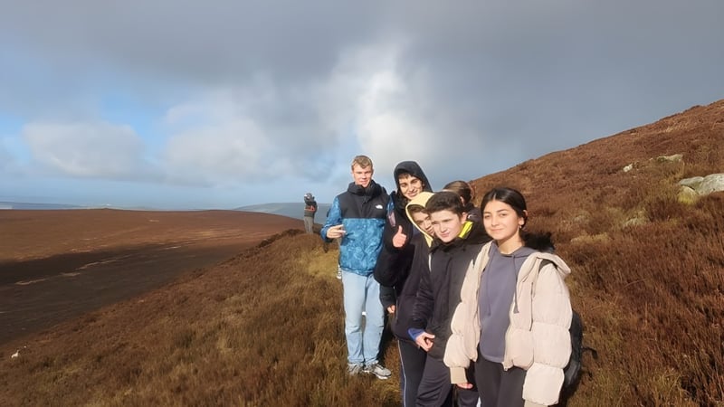 Eine Gruppe von Schülern des Duiske College steht auf einem naturbelassenen Wanderweg in einer hügeligen, grasbewachsenen Landschaft.