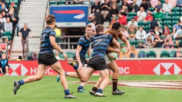Schüler von Dulwich College spielen ein Rugby-Match auf einem Rasenfeld mit Zuschauern im Hintergrund.