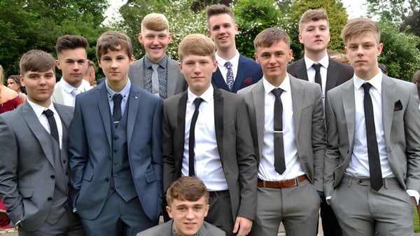Eine Gruppe Schüler des Dulwich College steht formell gekleidet im Freien vor Bäumen und Grünflächen.