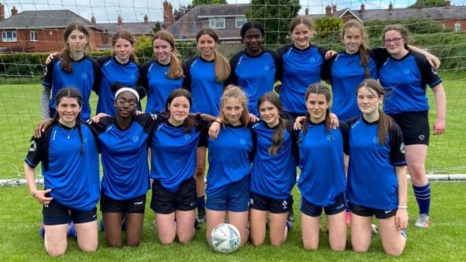 Eine Gruppe junger Fußballspielerinnen in blauen Trikots steht auf dem Sportplatz der Dundalk Grammar School.