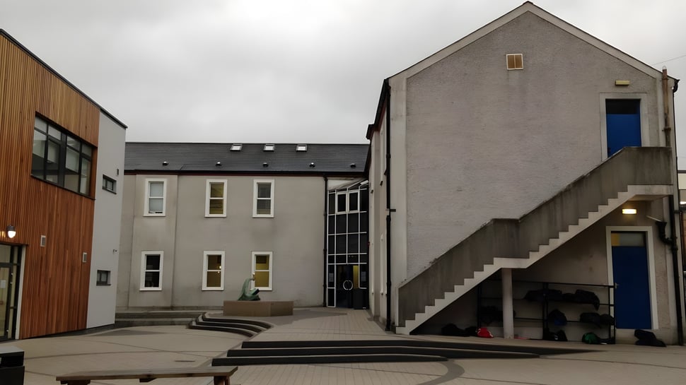 Das mehrstöckige Gebäude der Dundalk Grammar School mit grauer Fassade und einer blauen Eingangstür im Vordergrund ist zu sehen.