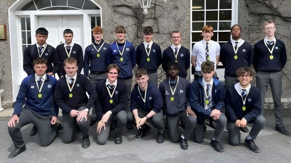 Eine Gruppe Schüler der Dundalk Grammar School steht vor einem Gebäude mit Steinfassade und rundbogigen Fenstern.