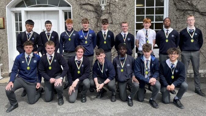 Eine Gruppe von Schülern in Schuluniformen steht vor einem Gebäude mit Rundbogenfenstern auf dem Campus der Dundalk Grammar School.