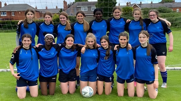 Eine Gruppe von Schülerinnen der Dundalk Grammar School steht zusammen auf einer Wiese vor Gebäuden und Bäumen.