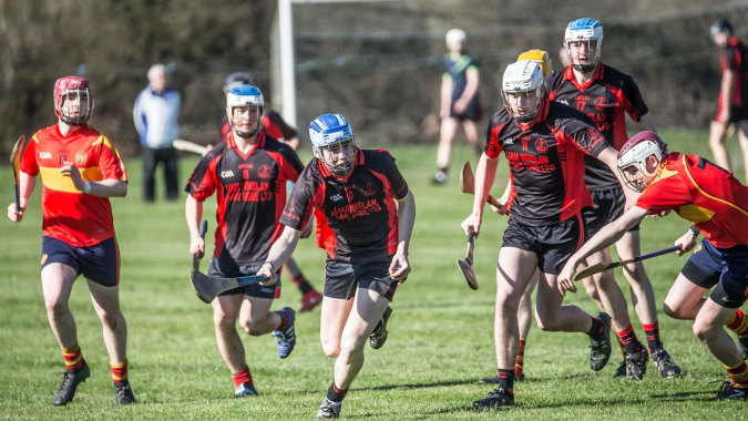 Eine Gruppe junger Athleten läuft auf dem Sportfeld des Dungarvan College in roten und schwarzen Uniformen.