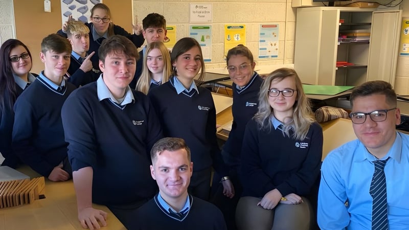 Schülerinnen, Schüler und Lehrkräfte des Dungarvan College posieren gemeinsam in einem Klassenraum mit Lernmaterialien im Hintergrund.