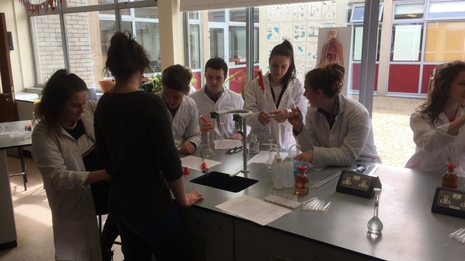 Eine Gruppe Schülerinnen und Schüler in weißen Kitteln arbeitet gemeinsam im Labor des Dungarvan College.