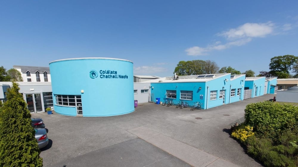 Das bunte und moderne Gebäude mit einem großen türkisfarbenen Wasserturm auf dem Campus des Dungarvan College umgeben von Grünflächen.