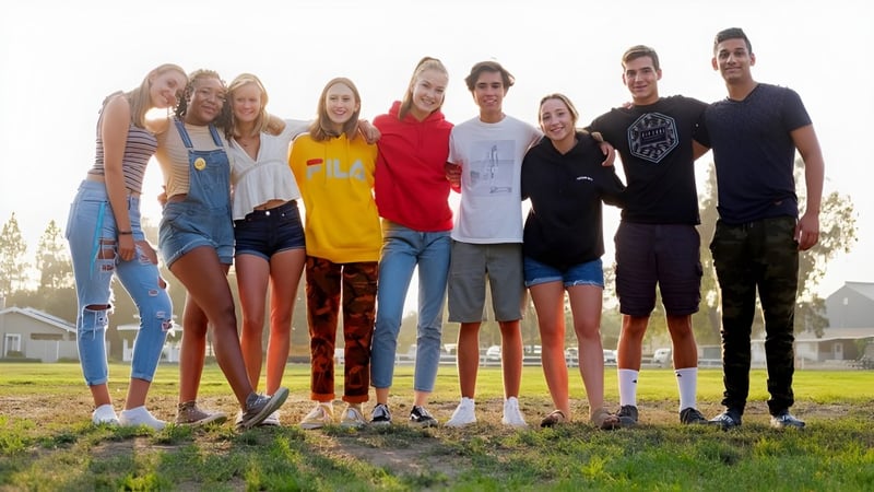 Eine Gruppe Schülerinnen und Schüler der Dunn School steht zusammen auf einer Wiese mit Häusern im Hintergrund.