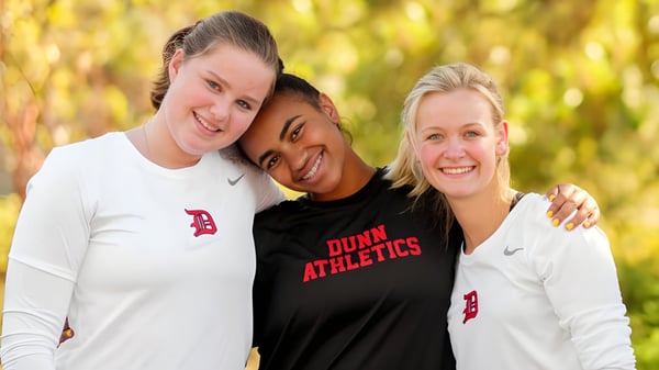 Drei Schülerinnen der Dunn School posieren draußen in Sportkleidung vor einem natürlichen Hintergrund.