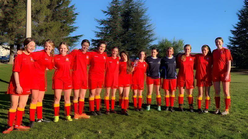 Eine Gruppe junger Fußballspielerinnen im roten Trikot steht auf einem Sportplatz der Dunstan High School.