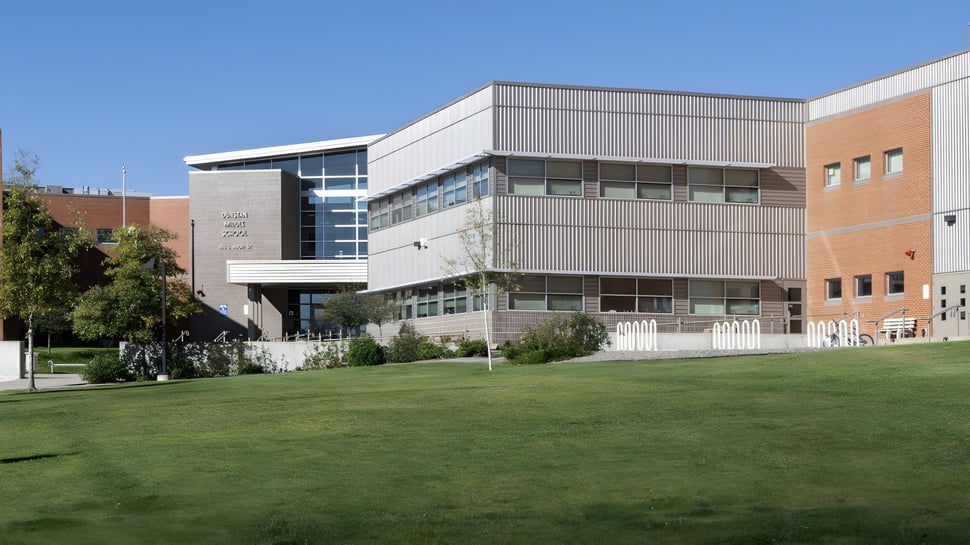 Das moderne Gebäudekomplex der Dunstan High School mit Glasfassade steht auf einem Grasfeld, umgeben von Bäumen.