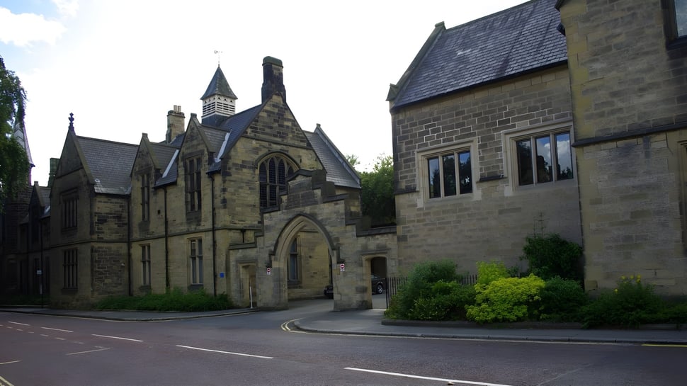 Das historische steinerne Hauptgebäude mit hohem Turm und reich verzierter Architektur der Durham School ist von Bäumen umgeben.