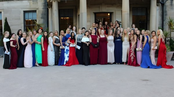 Eine große Gruppe Frauen in festlichen Abendkleidern steht vor einem prachtvollen Gebäude auf dem Gelände der Durham School.
