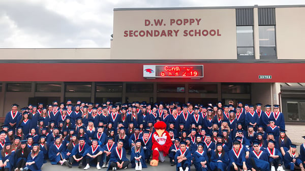 Eine Gruppe Schülerinnen und Schüler steht vor dem Gebäude der D.W. Poppy Secondary School.