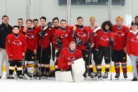 Schüler der D.W. Poppy Secondary School stehen in roten und schwarzen Trikots auf einer Eisfläche während eines Hockeyspiels.
