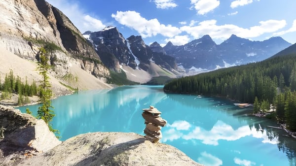 Blick auf einen türkisfarbenen Bergsee mit schneebedeckten Bergen und grünen Wäldern am D.W. Poppy Secondary School Campus.