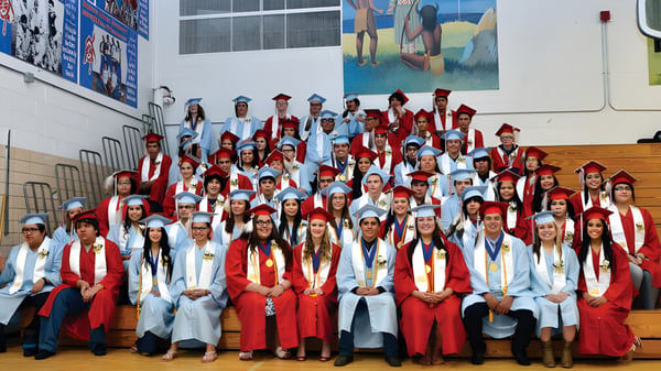 Absolventen der Eagle Butte High School in roten und weißen Talaren posieren vor einem farbenfrohen Wandbild.