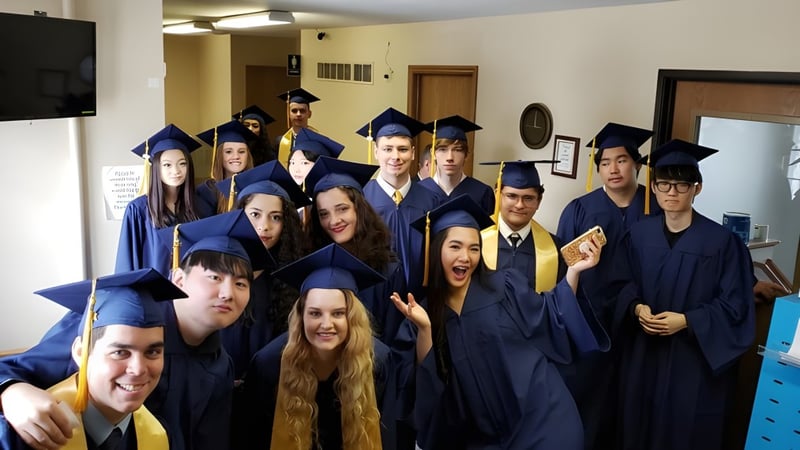 Eine Gruppe von Absolventinnen und Absolventen der Eagle School in blauen Abschlussroben in einem Raum mit Fernseher und Möbeln.