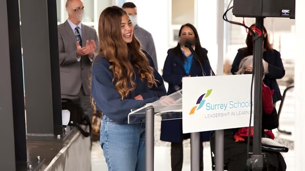 Eine Gruppe von Personen steht vor einem Schild mit der Aufschrift Surrey Service auf dem Gelände der Earl Marriott Secondary School.