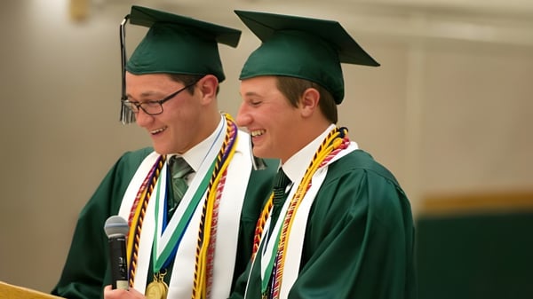 Zwei Männer in grünen Abschlussroben stehen zusammen und lächeln auf dem Campus der Earl of March Secondary School.