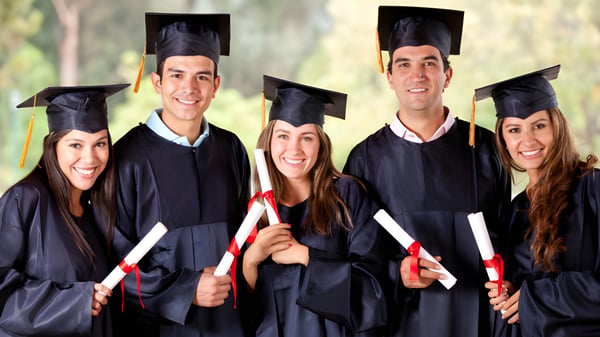 Eine Gruppe Absolventinnen und Absolventen des Earnshaw State College in schwarzen Talaren und Mützen steht zusammen vor einem natürlichen Hintergrund.