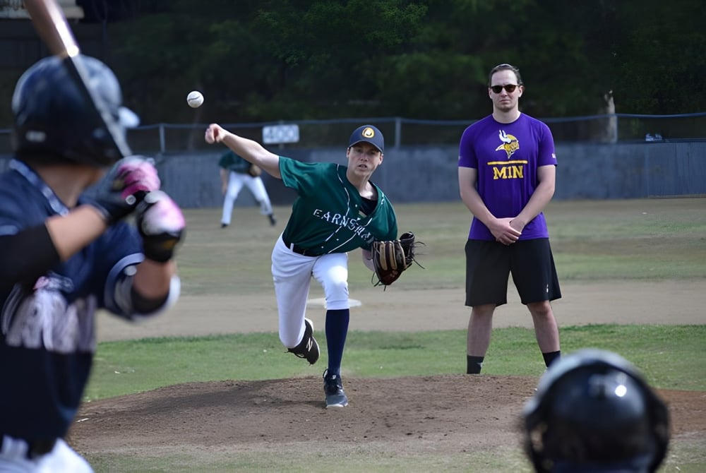 Ein Baseballspiel läuft auf dem Sportplatz von Earnshaw State College mit Pitcher, Batter und einem Coach während des Spiels.