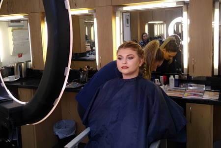 Eine Frau mit blonden Haaren steht vor einem Spiegel im Salon des East Sussex College Eastbourne.