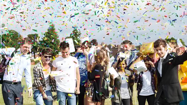 Schüler und Schülerinnen des East Sussex College Eastbourne feiern draußen unter buntem Konfetti mit Bäumen im Hintergrund.