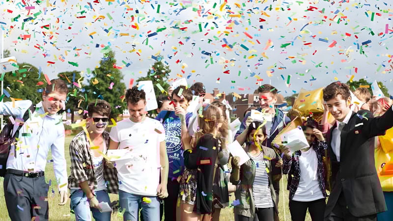 Schüler und Schülerinnen des East Sussex College Eastbourne feiern draußen unter buntem Konfetti mit Bäumen im Hintergrund.