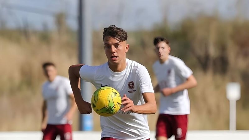 Ein Schüler des East Sussex College Hastings hält einen gelben Fußball auf einem Rasenfeld mit anderen Spielern im Hintergrund.