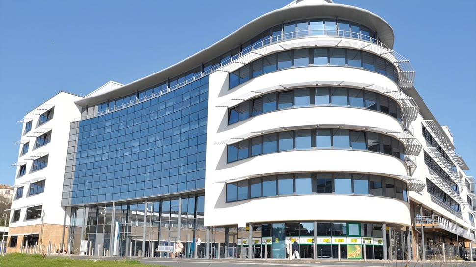 Das moderne mehrstöckige Gebäude des East Sussex College Hastings mit Glasfassade und geschwungener Architektur vor blauem Himmel.