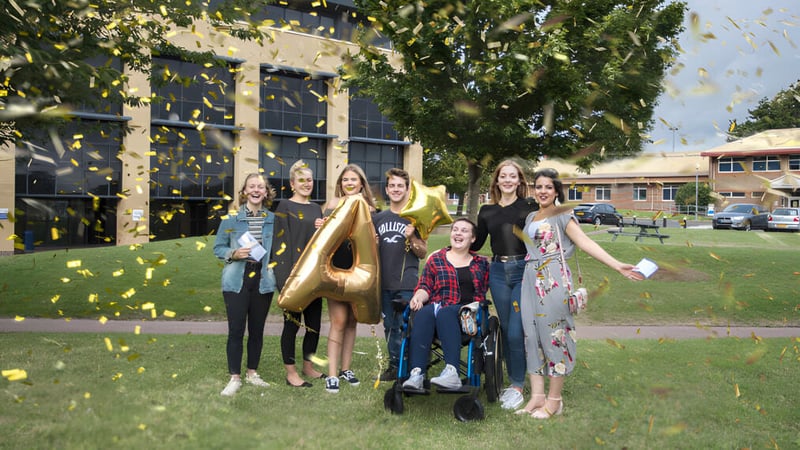 Eine Gruppe von Schülerinnen des East Sussex College Hastings posiert gemeinsam auf einer Wiese mit Bäumen und einem Gebäude im Hintergrund.
