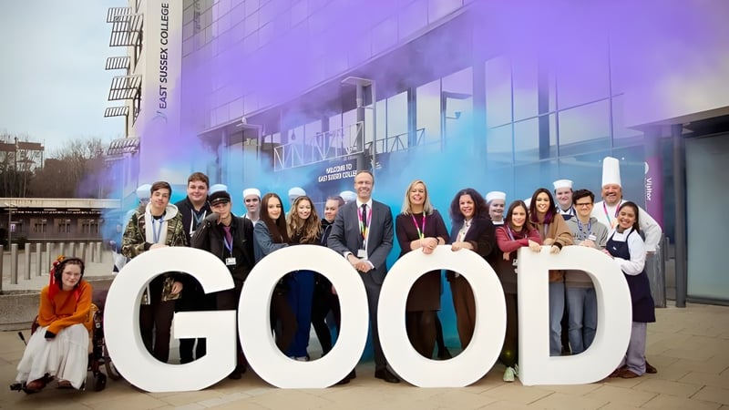Eine Gruppe von Schülerinnen und Schülern steht vor dem großen GOOD-Schild auf dem Campus des East Sussex College Lewes.