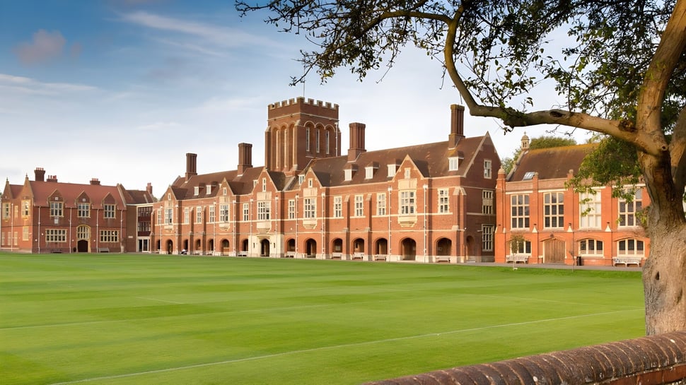 Das historische Backsteingebäude mit Türmen des Eastbourne College steht vor einem grünen Rasen und einem großen Baum.