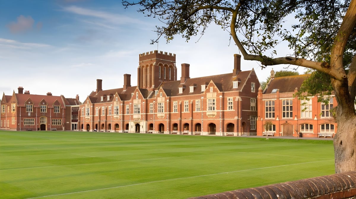 Das historische Backsteingebäude mit Türmen des Eastbourne College steht vor einem grünen Rasen und einem großen Baum.