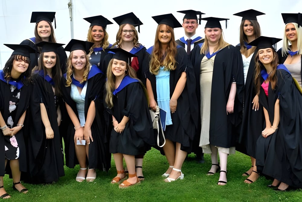 Eine Gruppe von Absolventen des Eastbourne College steht auf einer Wiese und feiert ihren Abschluss in akademischer Kleidung.