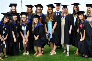 Absolventinnen und Absolventen des Eastbourne College stehen auf einer Wiese und feiern ihren Abschluss.