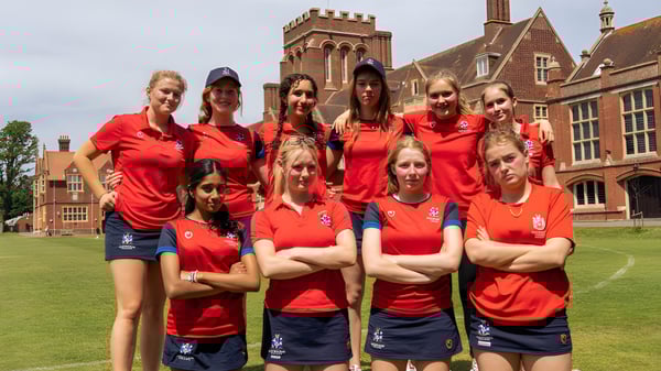 Eine Gruppe Schülerinnen in roten Uniformen steht gemeinsam auf dem Rasen vor einem historischen Gebäude auf dem Gelände des Eastbourne College.